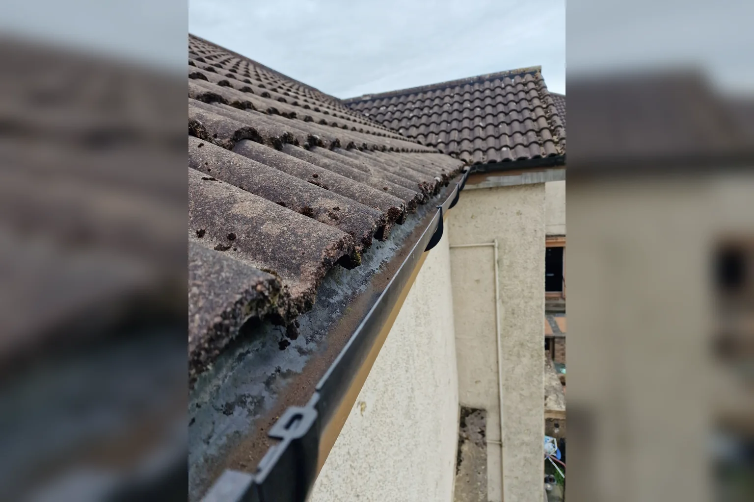 Roofline gutter with built-up debris before clearing.